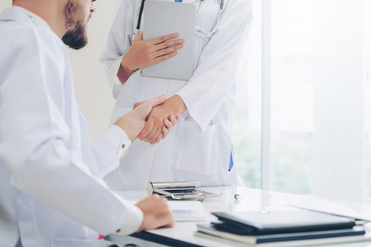 Doctor at the hospital giving handshake to another doctor showing success and teamwork of professional healthcare staff.