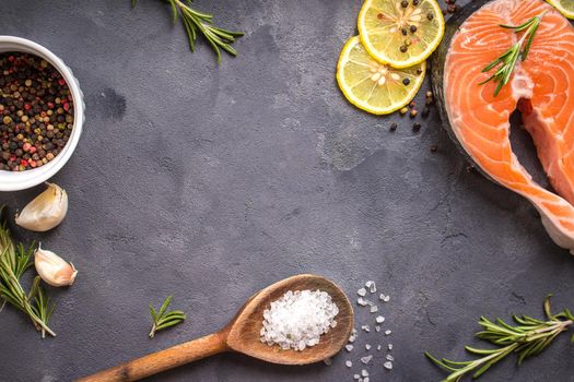 Fresh raw salmon steak, lemon, herbs, spices, wooden spoon on dark rustic concrete background. Food frame. Ingredients set for making healthy dinner. Healthy/diet concept. Space for text. Fresh fish