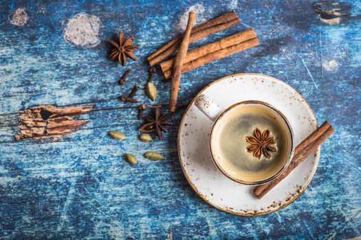 Cup of fresh hot coffee with spices on old rustic blue wooden table. Vintage background. Space for text. Autumn/winter warming coffee. Black coffee, cinnamon. Espresso, white cup. Top view. Close up