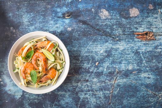 Homemade pasta with fried shrimps and basil on rustic wooden blue background. Space for text. Pasta with seafood in plate. Top view. Closeup. Mediterranean cuisine. Pasta for dinner or lunch. Overhead