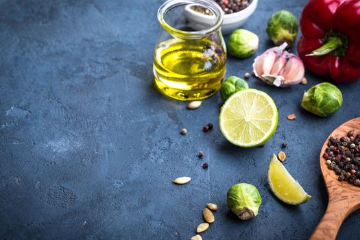 Ingredients for cooking. Olive oil in glass jar, wooden cooking spoon, spices, red bell pepper, lime, brussels sprout, garlic, colourful seasonings. Cooking ingredients background. Space for text