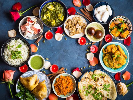 Festive food for Indian festival Diwali. Naan, samosa, rice, paneer, sweets. Background. Holiday Indian table with food, sweets, flowers, burning candles. Diwali celebratory dinner. Space for text.