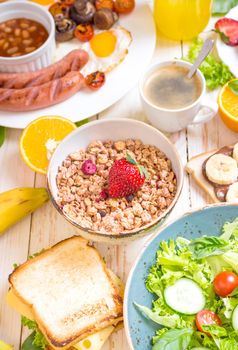 Assortment of breakfast choices. Granola with strawberry in a bowl and sausages, fried eggs, bacon, salad, cheese sandwich, pancakes, chocolate cream and banana toast, coffee, orange juice. Close-up