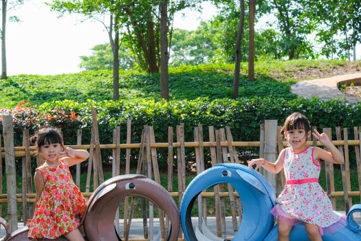 Cute little girl having fun in the outdoor playground. Young Asian sisters play together at school or kindergarten. Healthy summer activity for children.