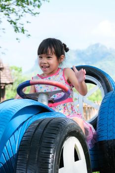 Cute little girl having fun in the outdoor playground. A young girl rides on a toy car made of old tires in the park. Healthy summer activity for children.