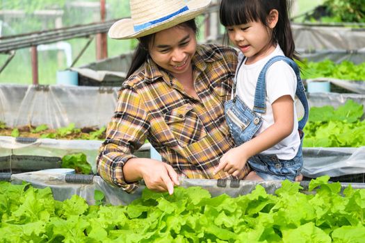 Young mother in straw hat teaching her daughters in backyard garden. Little girl helps her mother in the garden, a little gardener. Cute girl planting vegetables in the garden.