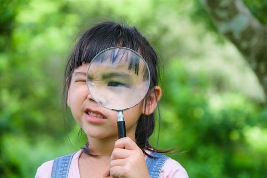 Cute little girl learning and exploring nature with outdoor magnifying glass. Curious child looks through a magnifying glass at a tree in the park. Little girl playing with a magnifying glass.