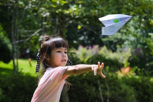 Happy children playing with paper airplane in the summer garden. Cute little girl throwing paper planes in the park. happy childhood concept.