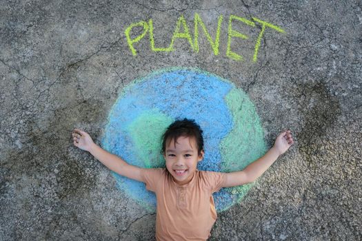 Cute little girl lying on a beautiful world painting with chalk labeled Planet on asphalt. Young volunteers do activities to save the world outdoors. Concepts of world environment day and peace day.