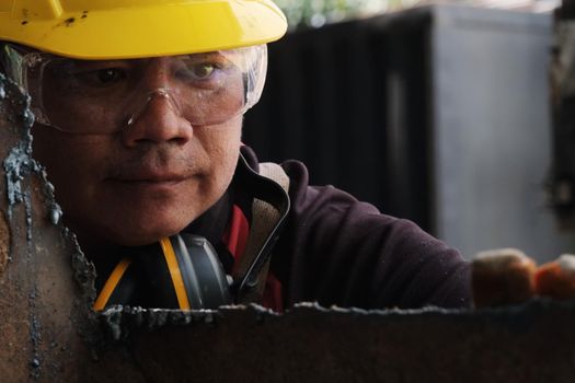 Male worker wearing goggles and construction gloves inspects the work after grinding metal with an angle grinder in home workshop.