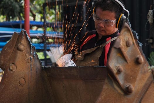 Man work in home workshop with angle grinder, goggles and construction gloves. Sanding metal makes sparks, closeup