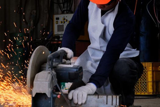 Professional men wearing goggles and construction gloves work in home workshop with electric steel cutter machine. Cutting metal makes sparks flying, closeup