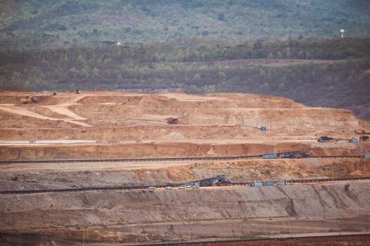 View of Trucks and excavators work in open pits in lignite coal mines. Lignite Coal Extraction Industry. The famous outdoor learning center of Mae Moh Mine Park, Lampang, Thailand.