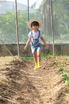 Little girl wearing a hat helps her mother in the garden, a little gardener. Cute girl playing in the vegetable garden.