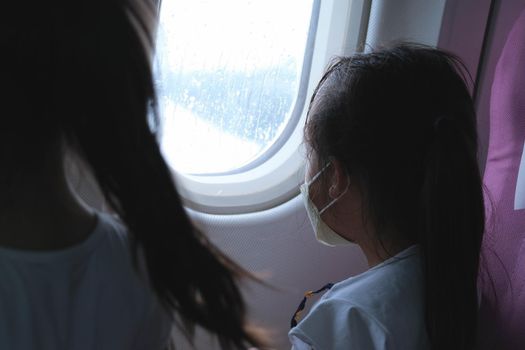 Child in airplane window seat. Two cute little sisters are watching the sky and clouds outside the plane window as they sit on the plane seat. Travel and family vacation.