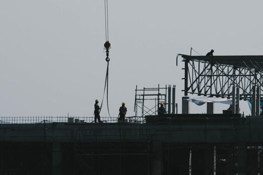 A large construction site with busy cranes. Tower cranes working on a construction site lifts a load at high-rise building in evening.