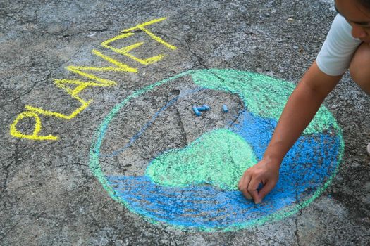 Young woman drawing with colorful chalk on asphalt.  Asian woman paints a beautiful world with the message Planet on courtyard. Concept of world environment day.