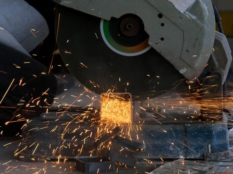 Professional men wearing goggles and construction gloves work in home workshop with electric steel cutter machine. Cutting metal makes sparks flying, closeup