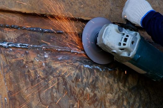 Professional men wearing goggles and construction gloves work in home workshop with angle grinder. Sanding metal makes sparks, closeup