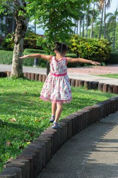 Cute little girl walking on the curb in the park. Young girl balancing