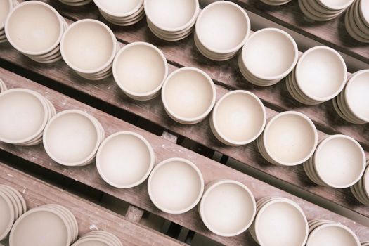 Many small round plates made of ceramic clay. Ceramic cup in rack prepare for painting design on surface in pottery workshop. handicraft and small business concept.