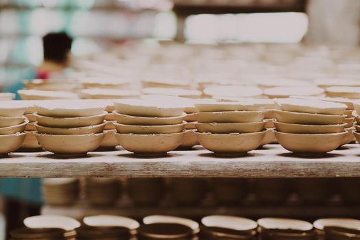 Many small round plates made of ceramic clay. Ceramic cup in rack prepare for cleans with sandpaper before applying the pattern on the clay product. handicraft and small business concept.