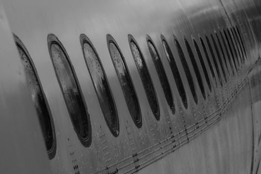 View of the plane's fuselage and many windows soaked in the rain.