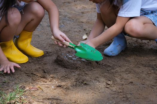 Cute little sisters in boots are using garden tools shovels for planting plants in the garden. A child helps mom in the garden, a little gardener.