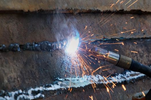 Closeup of a welding machine in work. Worker welds metal with sparks flying.