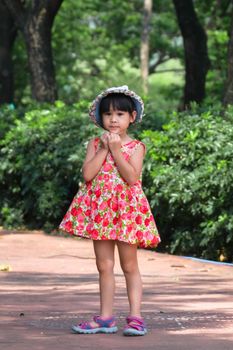 A cute smiling little girl in a red floral dress is walking and having fun on the green grass in the park. childhood concept