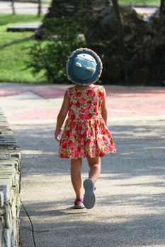 A cute smiling little girl in a red floral dress is walking and having fun on the green grass in the park. childhood concept