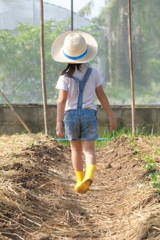 Little girl wearing a hat helps her mother in the garden, a little gardener. Cute girl playing in the vegetable garden.