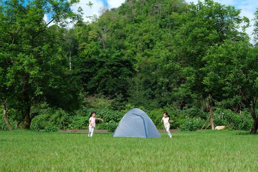 Happy little sisters play together in a campsite during summer vacation in the countryside. Two cute little girls having fun playing outdoors on a hot summer day. Happy childhood concept.