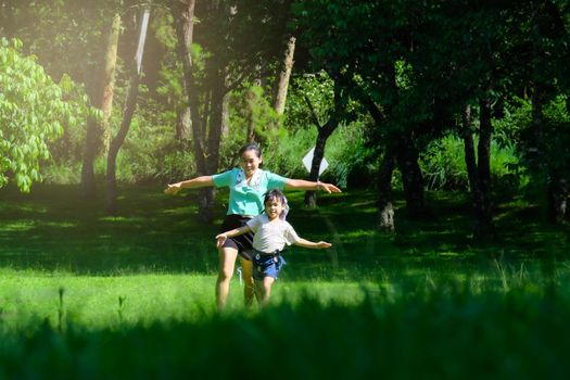 Cute little girl runs with her mother spreading her arms as if flying in a spring garden. Young mother playing with her daughter in the park. Happy family having fun in the park.