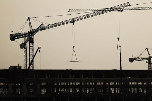 A large construction site with busy cranes. Tower cranes working on a construction site lifts a load at high-rise building in evening.