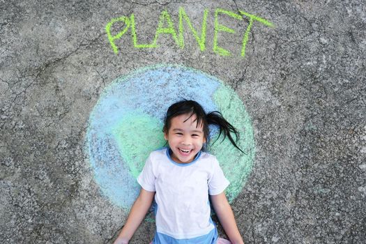 Cute little girl lying on a beautiful world painting with chalk labeled Planet on asphalt. Young volunteers do activities to save the world outdoors. Concepts of world environment day and peace day.