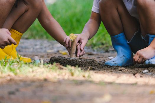Cute little sisters in boots are using garden tools shovels for planting plants in the garden. A child helps mom in the garden, a little gardener.
