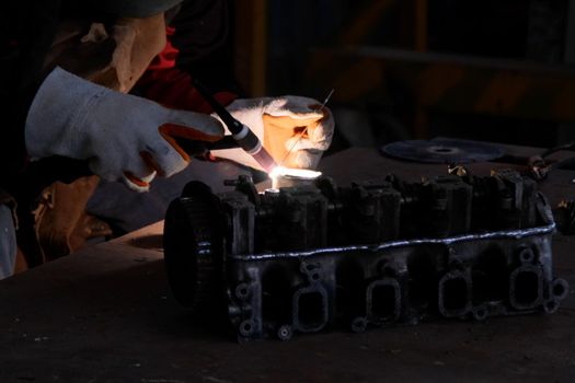 Professional men wearing welding mask and gloves work in home workshop with arc welding and argon.