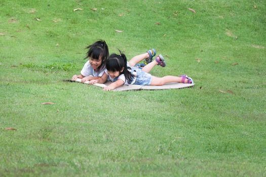 Two smiling little sisters lie prone on cardboard boxes sliding down the hill at the Botanical Gardens. The famous outdoor learning center of Mae Moh Mine Park, Lampang, Thailand. Happy childhood conc