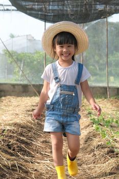 Little girl wearing a hat helps her mother in the garden, a little gardener. Cute girl playing in the vegetable garden.