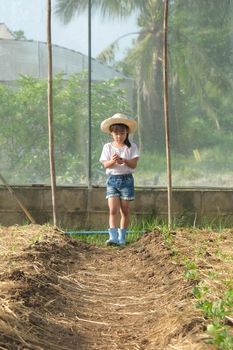 Little girl wearing a hat helps her mother in the garden, a little gardener. Cute girl playing in the vegetable garden.