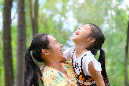 Young mother hugging with her daughter in the park. Smiling little girl playing with mother in summer park. Happy family having fun in the park.