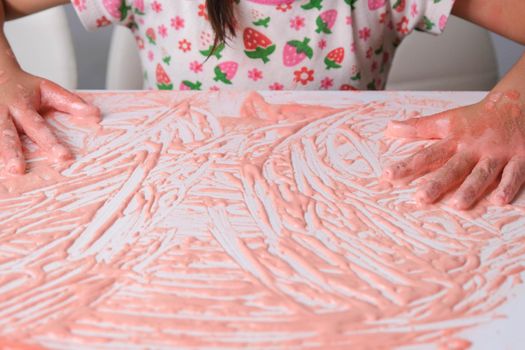 Little girl paints on a white table with colored salt, close up. Colored salt art. DIY Play and Learn Activities for Kids.