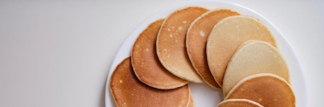 Lot of delicious appetizing pancakes lying on white plate in circle top view. Flour recipes concept