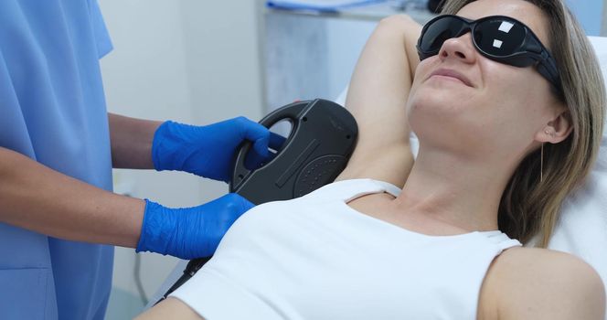 Woman client in protective glasses having laser hair removal of armpit in beauty salon 4k movie. Body care concept