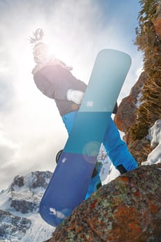 Beautiful young female snowboarder with blue snowboard and funny hat on the mountains. Look at camera. lens flare effect