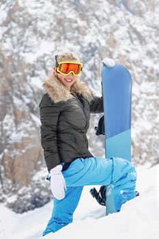Portrait of active female snowboarder standing on top of the mountain background. Copy space, vertical