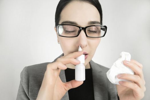 Young woman in glasses, uses nasal spray.