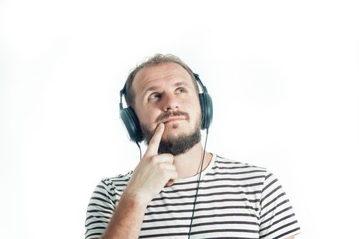 Meditative bearded happy man in a striped T-shirt listens to music with big headphones. 30-35 years old. Isolated on white