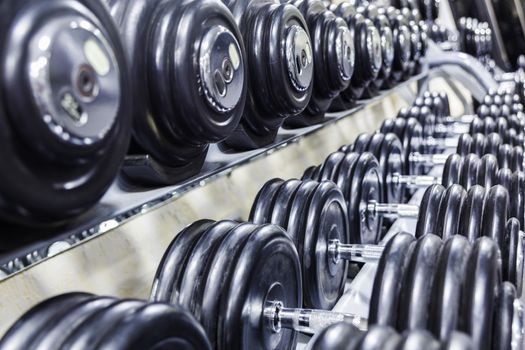 Black dumbbell set. Close up many rubberized dumbbells on rack in sport fitness center , Weight Training Equipment concept